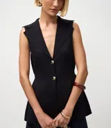 Chaleco negro de tejido punto, sin mangas, con cuello solapa y cierre frontal de dos botones dorados. El corte es acinturado y alargado.