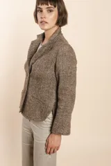 Chaqueta color crema de corte recto con cuello, solapa y bolsillos ojal. Forro solo en las mangas y terminaciones envivadas. Esquinas redondeadas y mangas con corte en puño que permiten transformarla en manga 3/4. Más larga en la espalda que en la delantera. Abrochadura con dos botones.