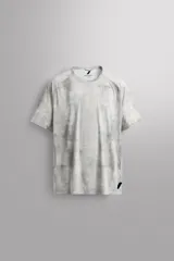 Camiseta de entrenamiento regular fit de Zara Athleticz, confeccionada en tejido técnico ligero y elástico con tecnología Quick Dry nivel 2. Presenta un estampado tipo tie-dye en tonos grises y blancos, cuello redondo, manga corta, costuras planas y termofijadas, y logo estampado en el bajo.