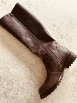 Bota de caña alta color marrón de cuero, con hebilla dorada y suela track.