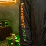Campera negra tipo windbreaker con capucha, cierre frontal y puños elásticos. Logo de Kaboa en el pecho y estampado con el logo de Jägermeister en la manga.