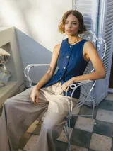 Chaleco de denim azul con escote en V, botones dorados y ribete de cuentas en el cuello.