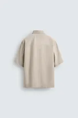 Camisa beige de corte relaxed fit, confeccionada en tejido con algodón, cuello solapa y manga corta.