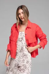 Campera corta color coral con cuello camisero, cierre frontal con botones, bolsillos de parche en el pecho y mangas largas con puños abotonados. Presenta calados tipo broderie en hombros, mangas y espalda.