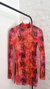 Vestido corto de microtul elastizado con estampado floral en tonos naranja, rosa y negro. Tiene cuello alto y mangas largas acampanadas.