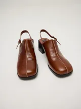 Mocasines de cuero color marrón con taco de madera y correa trasera ajustable.