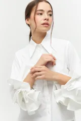 Camisa color beige con cuello clásico, mangas largas con volados en los puños y cierre frontal con botones.