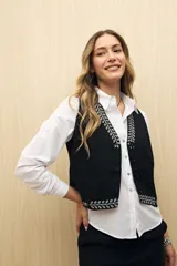 Chaleco negro con bordado floral blanco en el borde, con botones y corte clásico.