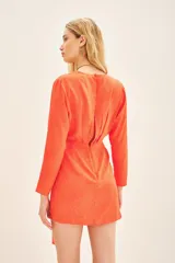 Vestido corto naranja vibrante de manga larga, confeccionado en viscosa jacquard con un sutil patrón en relieve. Presenta un escote cruzado tipo wrap y un detalle de falso nudo drapeado en la cintura que cae como un lazo asimétrico.