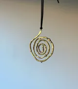 Collar con dije irregular hecho a mano en bronce con forma de espiral y cordón de gamuza negro.