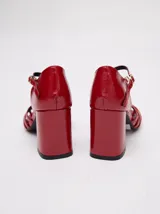 Sandalias negras de charol con tiras cruzadas en el empeine, pulsera con hebilla al tobillo y tacón cuadrado.