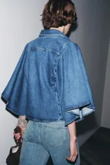 Camisa de denim azul con cuello solapa y mangas amplias tipo kimono. Tiene efecto lavado y cierre frontal con botones ocultos.