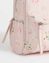 Mochila pequeña de cuerina color crema con estampado de flores pequeñas en tonos rosa, naranja y celeste. Tiene un bolsillo frontal con cierre, correas regulables, manija superior, cierre superior y bolsillos laterales.
