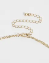 Collar corto doble dorado con dije ovalado blanco con corazón dorado y strass.