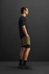 Shorts deportivos color verde oliva con calza interior negra, de tejido técnico ligero y elástico. Cuenta con cintura elástica ajustable con cordón, bolsillos laterales con cierre de cremallera, bajo con aberturas laterales y detalle de logo estampado.