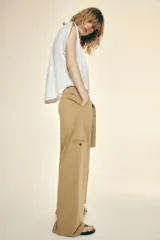 Pantalón color beige de tiro alto con cinturón ajustable con hebilla metálica. Presenta bolsillos laterales, de vivo en la pierna y de parche en la espalda.