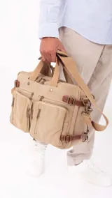 Mochila de tela canvas color beige con detalles en cuero marrón. Cuenta con múltiples bolsillos con cierre, compartimento acolchado para notebook y correas ajustables.