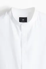 Camisa blanca de corte estándar, con cuello mao, tapeta clásica, canesú en la espalda, mangas largas con puños abotonados y bajo redondeado.