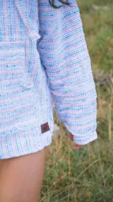 Buzo con capucha de tejido tipo poncho, con diseño a rayas horizontales en tonos celeste, rosa y blanco.