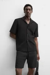 Camisa color crudo de corte regular fit, confeccionada en tejido con textura. Tiene cuello bowling, manga corta, bajo con aberturas laterales y cierre frontal con botones.