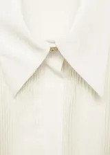 Camisa color crema de tejido fluido con cierre de botones oculto, cuello camisero, panel frontal con textura plisada, corte recto y mangas largas abotonadas.