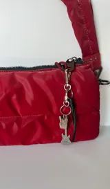Llavero rojo acolchado con dijes colgantes de mano haciendo cuernitos y una guitarra eléctrica.