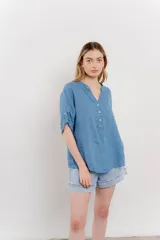 Camisa azul de lino con escote en V abotonado, bolsillo frontal y mangas 3/4 con trabilla.