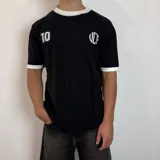 Remera tejida blanca con cuello y puños negros, con el número 10 estampado en la espalda en color negro. Incluye las siglas VCP y el rango de años 2015-infinito.