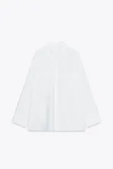 Camisa blanca de corte holgado, con cuello solapa, manga larga con puños y dos bolsillos con solapa en el pecho.