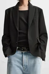 Blazer negro de corte regular fit, confeccionado en tejido con viscosa. Presenta cuello con solapas de muesca, manga larga con puños abotonados, bolsillo de vivo en el pecho, bolsillos de solapa en la cadera, bolsillo interior, aberturas en la espalda y cierre frontal con dos botones.