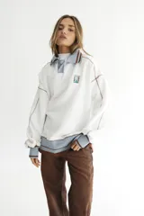 Buzo celeste con cuello polo y puños en rib color verde lima. Tiene un parche con el logo de la marca en el pecho y rayas horizontales en el ruedo.