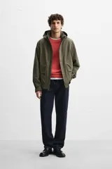 Parka verde militar confeccionada en tejido técnico ligero resistente al viento, con cuello alto, capucha, manga larga con puños ajustables, bolsillos de plastrón con solapa en la cadera, bolsillo interior, bajo ajustable con elásticos y cierre frontal con cremallera oculta por solapa con botones a presión.