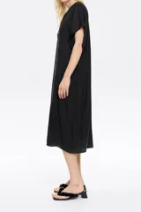 Vestido midi negro de corte recto, con escote en V pronunciado en delantero y espalda, manga corta recta con bajo descosido, cierre frontal con botonadura y fruncidos laterales en el bajo.