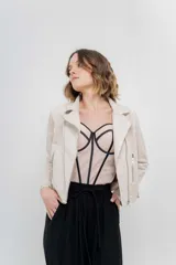 Chaqueta color beige de tela tipo gamuza con elastano, cuello solapa, manga larga con trabillas en hombro, bolsillos delanteros con cremallera metálica y cierre frontal con cremallera.