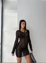 Vestido corto de punto calado color negro, con cuello redondo y mangas largas. Presenta un diseño semi-transparente de silueta ajustada.