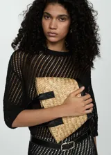 Clutch de mano confeccionado en rafia natural trenzada, con detalles en cuero negro en los bordes y en las asas.