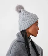 Gorro de lana gris con textura trenzada, dobladillo acanalado y pompón de piel sintética en la parte superior.