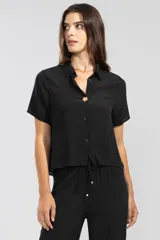 Camisa negra de manga corta en crepé de viscosa suave, con cuello camisero y detalle de flor en la botonadura central.