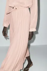 Vestido midi de color rosa pálido con falda plisada, cuello redondo, manga larga y cinturón fino.