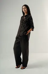 Camisa negra de manga larga con estampado de lunares blancos pequeños. Presenta cuello camisero, botones frontales y un bolsillo de parche en el pecho.