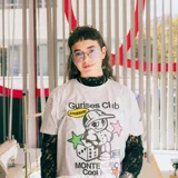 Remera blanca de algodón con corte boxy y estampado con el logo de Gurises Club, que incluye un personaje de caricatura, estrellas, un dado y la inscripción 'Montevideo Cool Kids'.