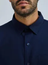 Camisa de vestir azul marino, de corte clásico, con cuello abotonado, manga larga y bolsillo en el pecho.