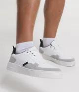 Championes urbanos de cuero sintético blanco con recortes en gris y negro, cierre con cordones y suela de goma.