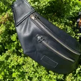 Riñonera negra con textura tipo piel de cocodrilo, con tres compartimentos con cierre y correa ajustable.