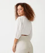 Blusa cropped blanca de laise texturizado con mangas 3/4 ajustadas y lazo en el bajo.