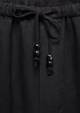 Pantalón negro de lino con diseño crop y jogger, tiro medio, cintura elástica con lazo, dos bolsillos laterales y dos bolsillos de ribete en la parte posterior.