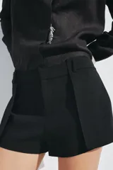 Shorts negros de tiro medio con cintura con trabillas y pliegues delanteros. Cierre frontal con cremallera, botón y ganchos metálicos.