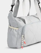 Bolso deportivo acolchado color celeste con bolsillo frontal con cierre, correa regulable y desmontable, y manija superior.