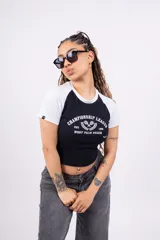 Remera corta blanca con mangas raglán negras, cuello redondo y estampado frontal con el texto "Championship League Est. 1996 West Palm Beach" y dos raquetas de tenis cruzadas.