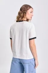 Remera color crudo de manga corta con cuello y puños negros. Estampa frontal con texto "Côte D'Azur" y dibujo de playa con palmeras.